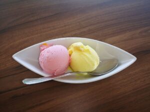 Delicious strawberry and lemon ice cream scoops served in a white bowl with a spoon on wooden table.